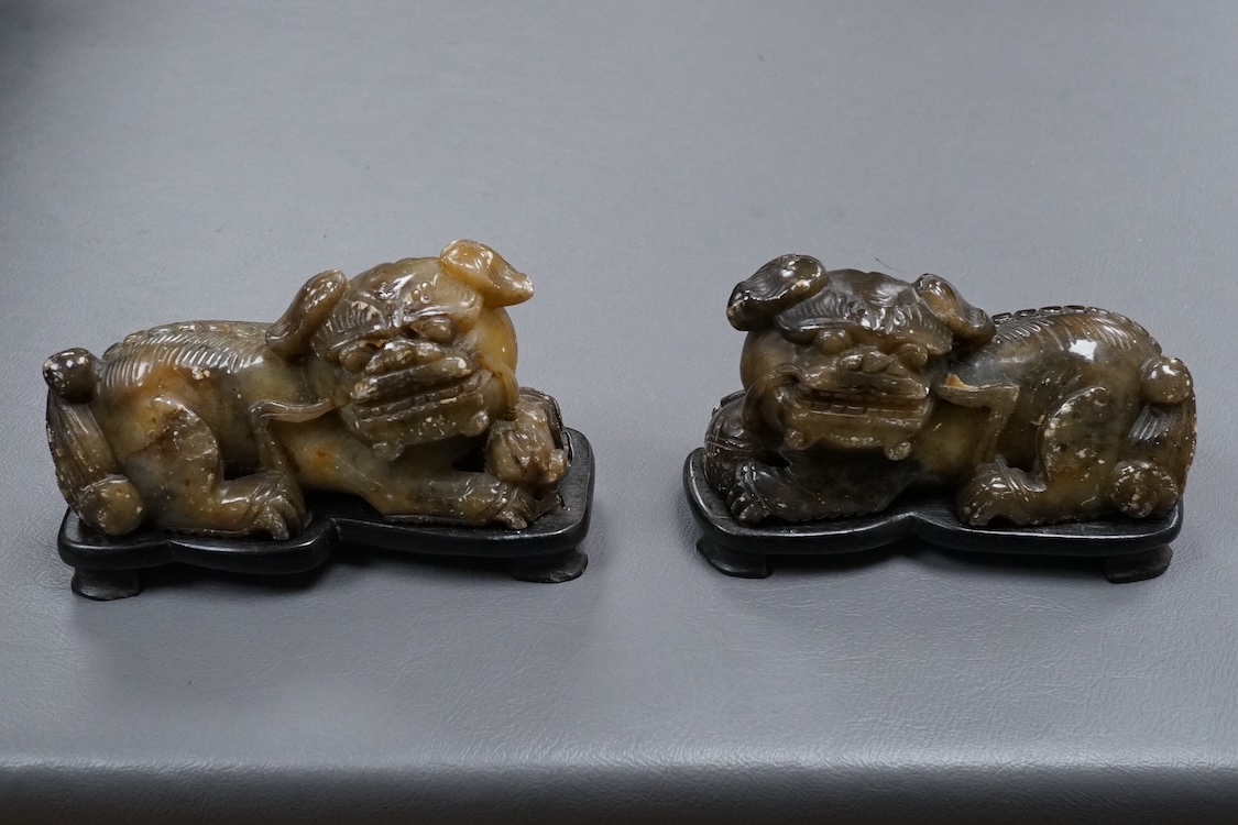 A pair of Chinese soapstone figures of lion dogs, on wood stands, 11cm wide